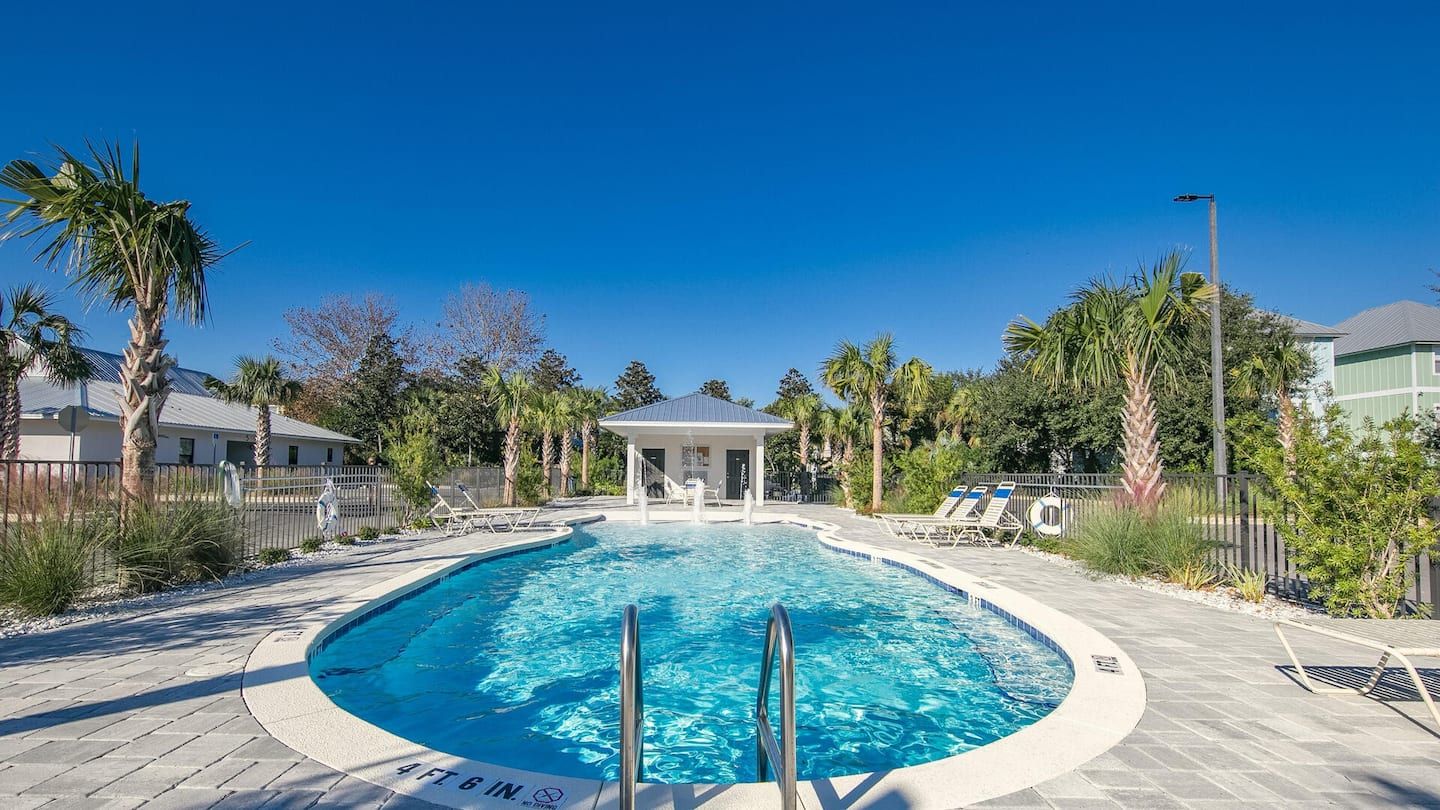 Community pool with gazebo and lounge chairs surrounded by palm trees